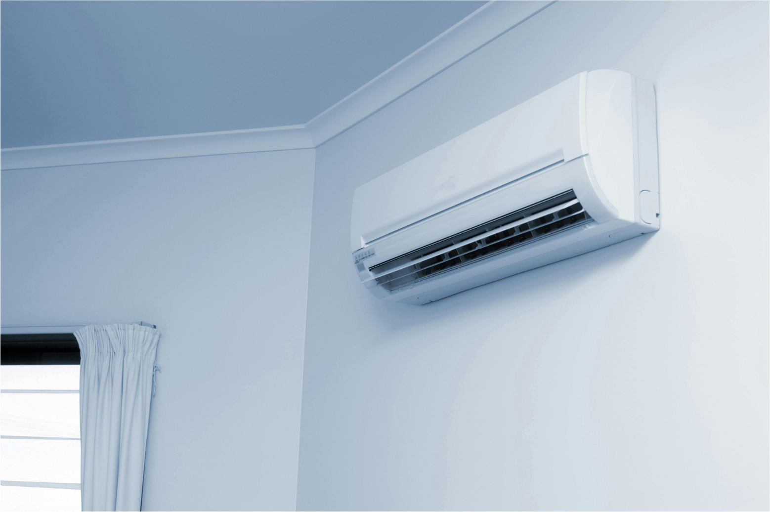 Wall-mounted white air conditioner above a window in a light blue room