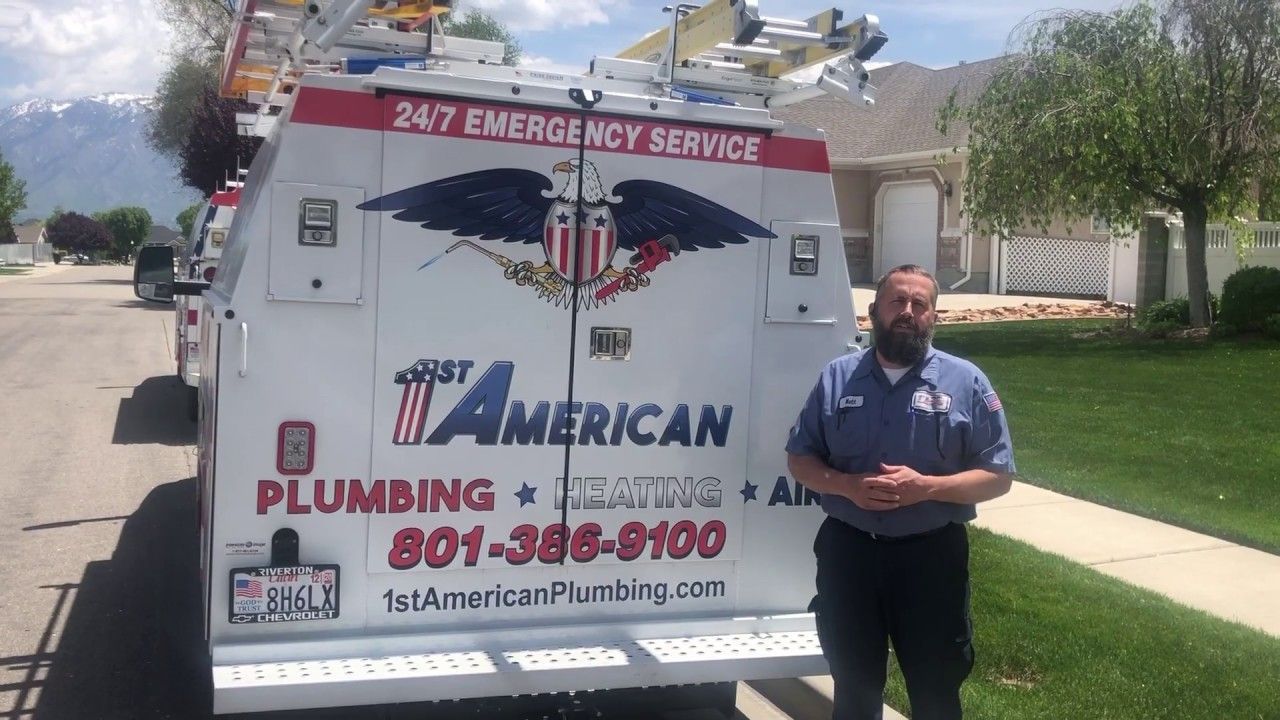 Plumbing service truck parked on a suburban street with a man standing beside it.