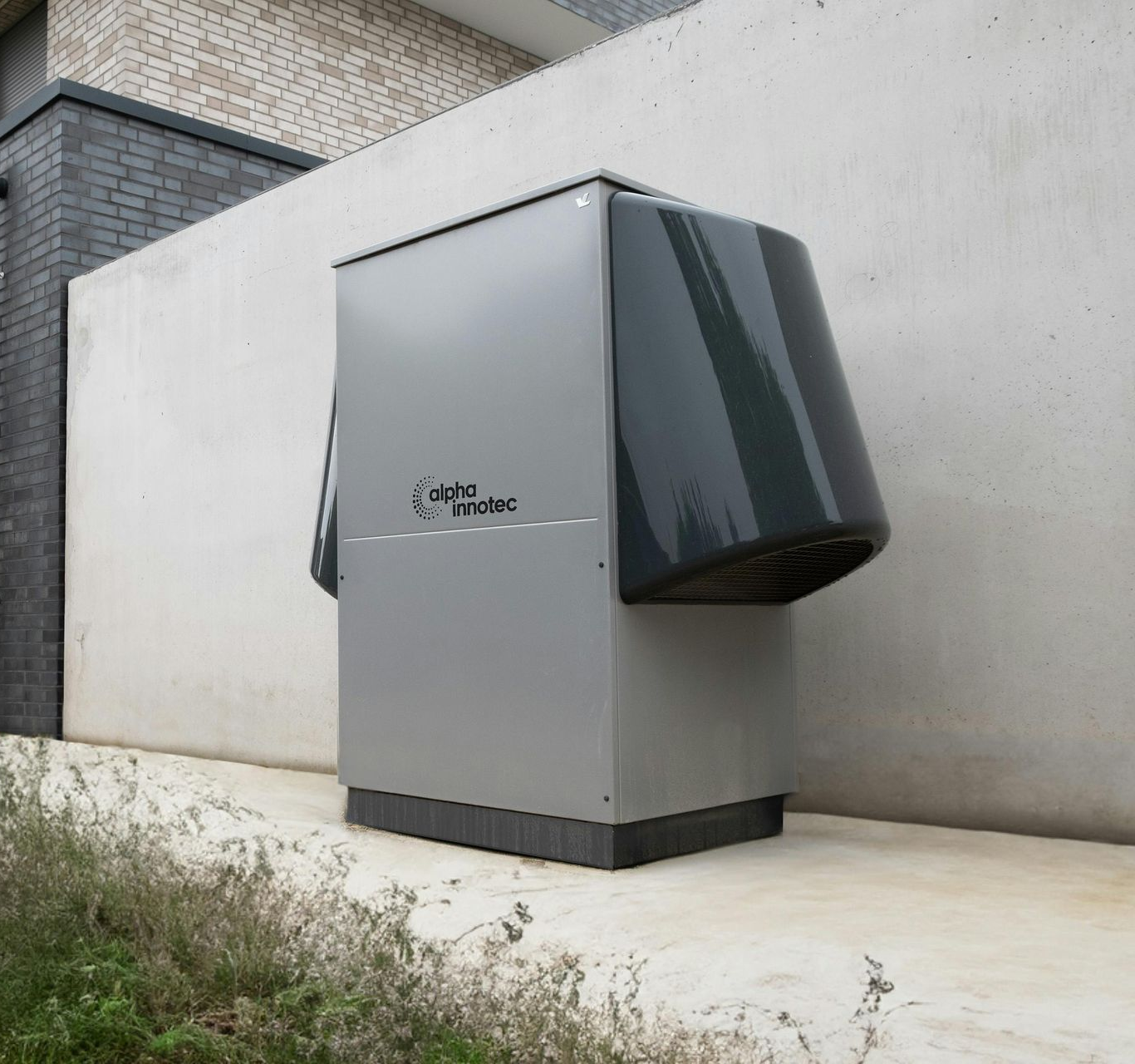 Large gray industrial unit with dark side panels installed outdoors beside a concrete wall.