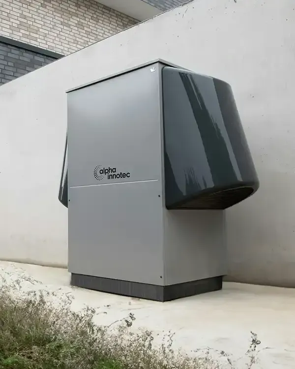 Large gray industrial unit with dark side panels installed outdoors beside a concrete wall.