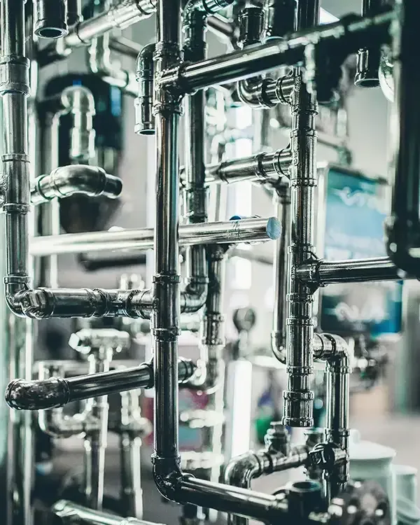 Industrial metal piping and valves in a bright mechanical facility, with reflective stainless-steel tubes.