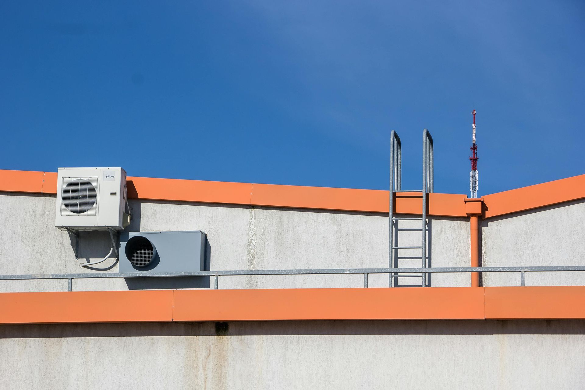 Rooftop with air-conditioning units, ladder, and orange trim against a blue sky