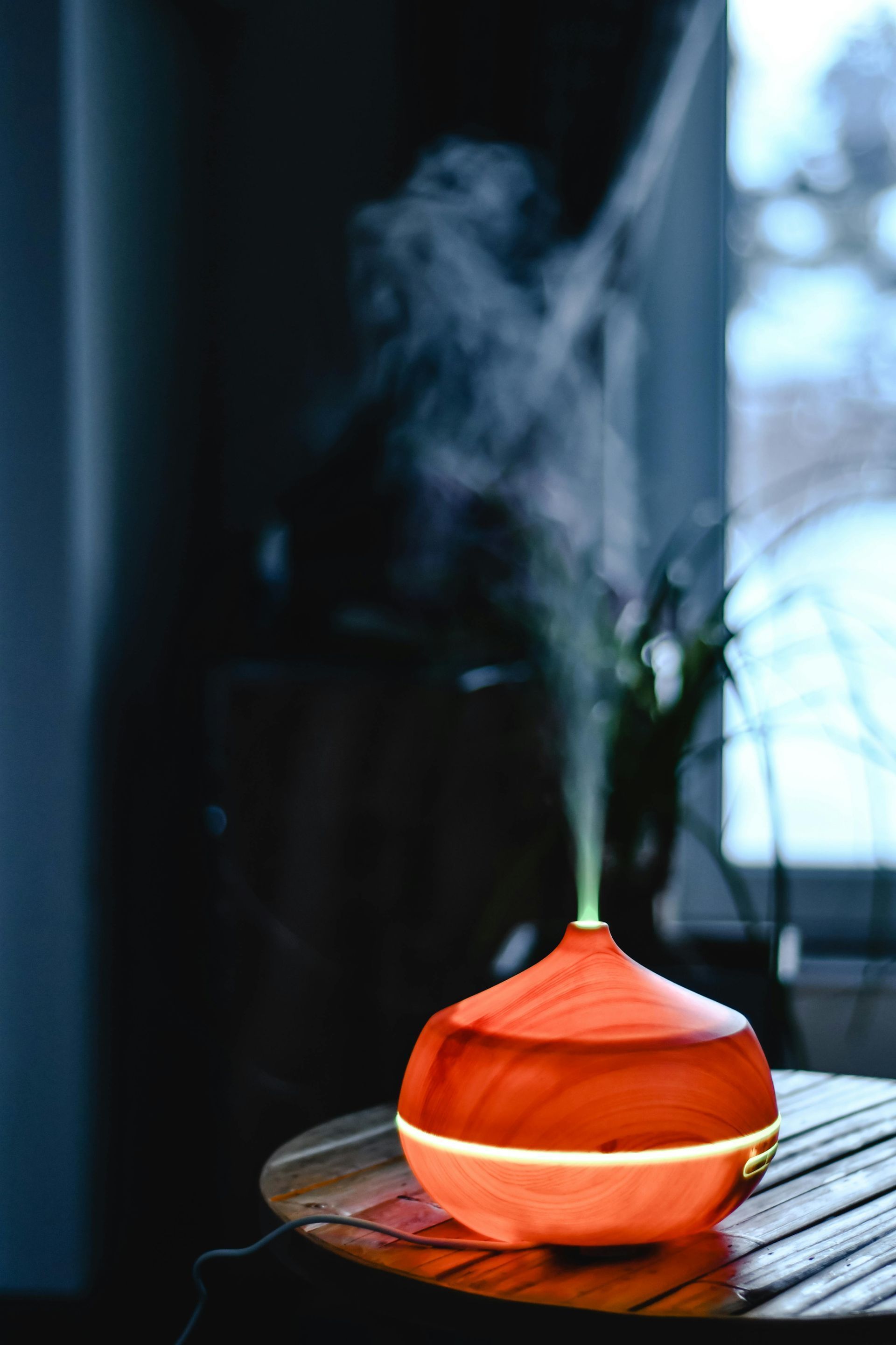 Orange essential oil diffuser emitting steam on a table by a window