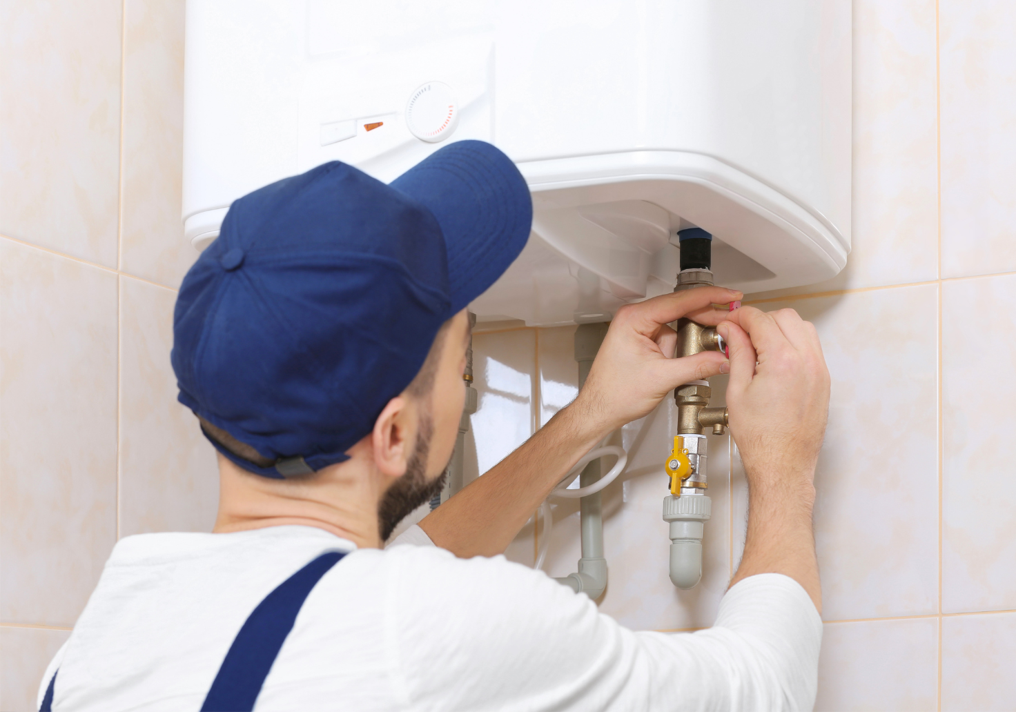 Technician repairing a wall-mounted water heater with tools in a tiled bathroom