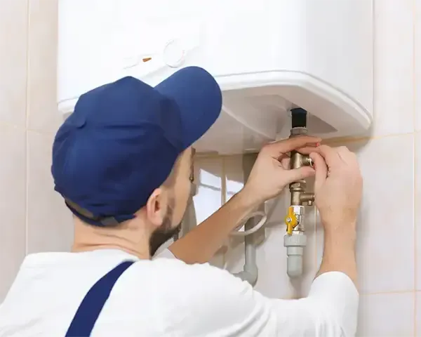 Technician repairing a wall-mounted water heater with tools in a tiled bathroom