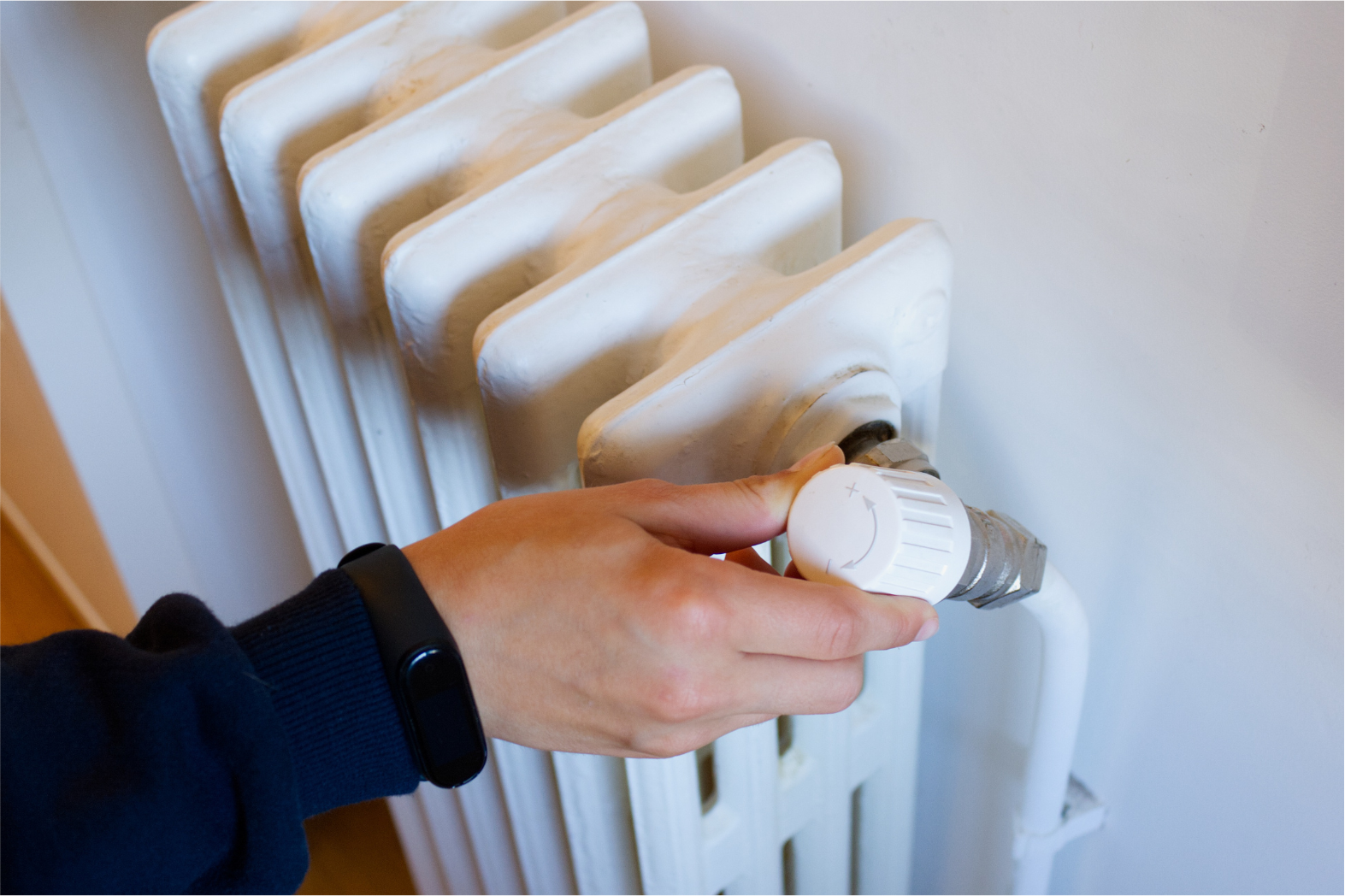 Hand turning a white radiator valve to adjust heat