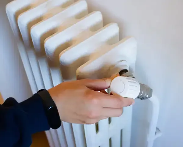 Hand turning a white radiator valve to adjust heat