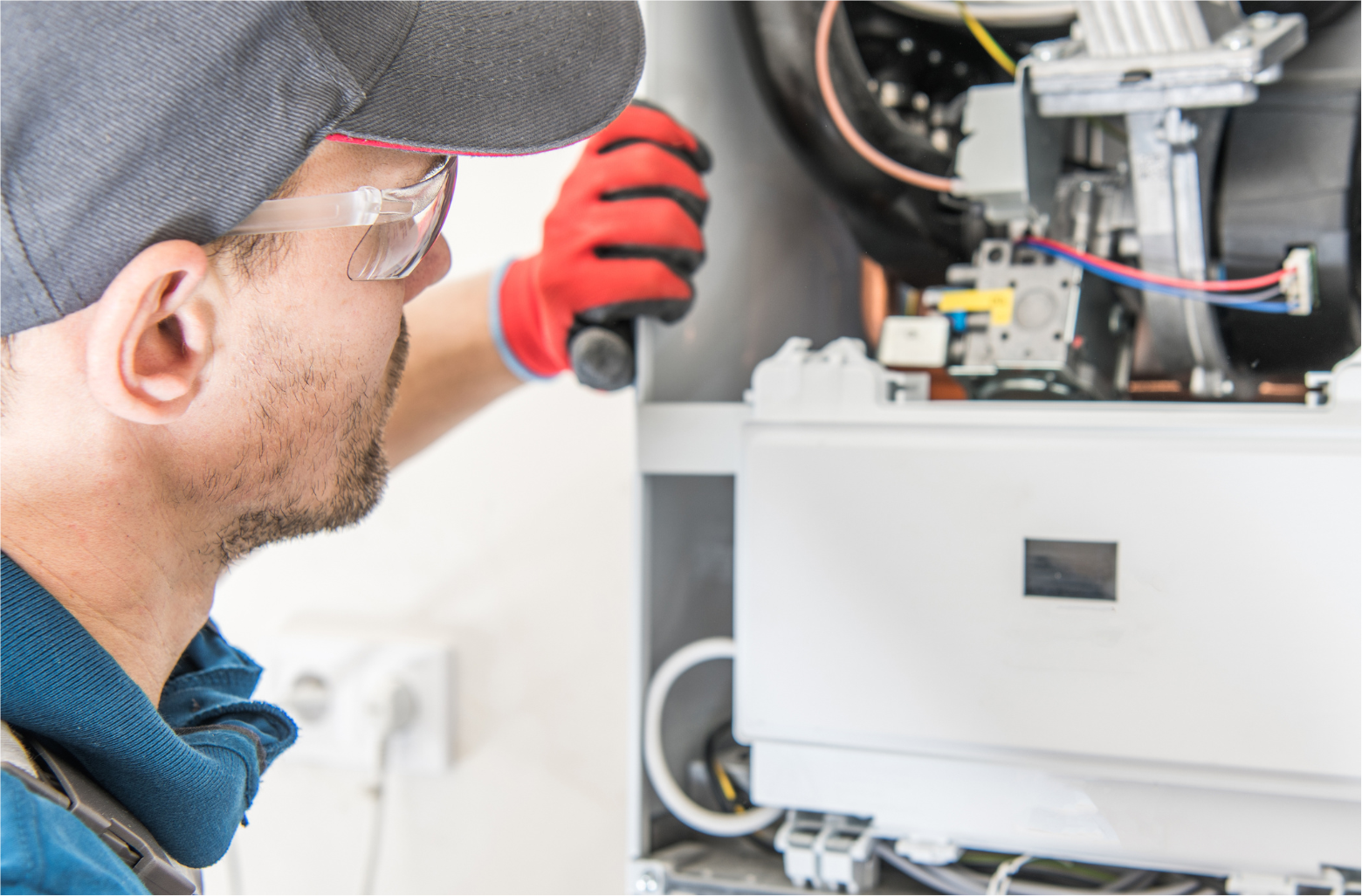 Technician in cap and gloves inspecting electrical equipment inside a control panel