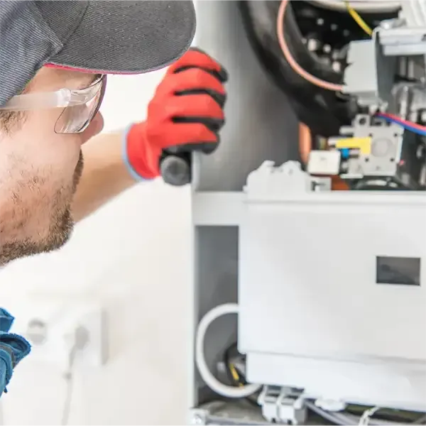 Technician in cap and gloves inspecting electrical equipment inside a control panel