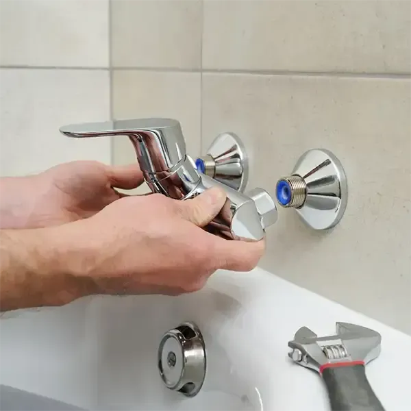 Hands using pliers to fix a chrome pipe on a workbench with scattered tools and fittings