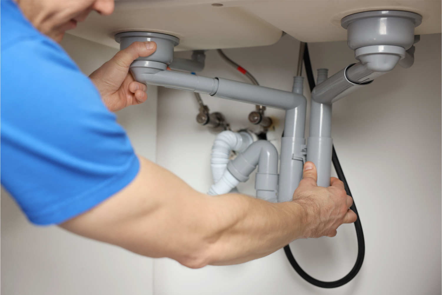 Hands using pliers to fix a chrome pipe on a workbench with scattered tools and fittings