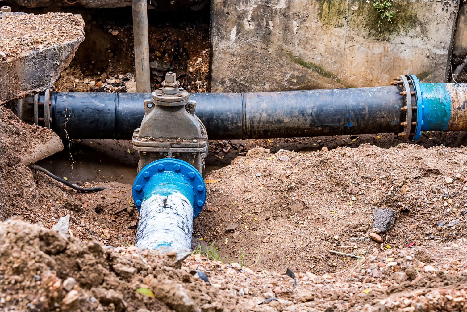 Underground water pipe with blue fittings and a valve in a dirt trench