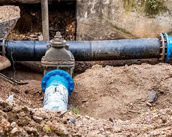 Underground water pipe with blue fittings and a valve in a dirt trench