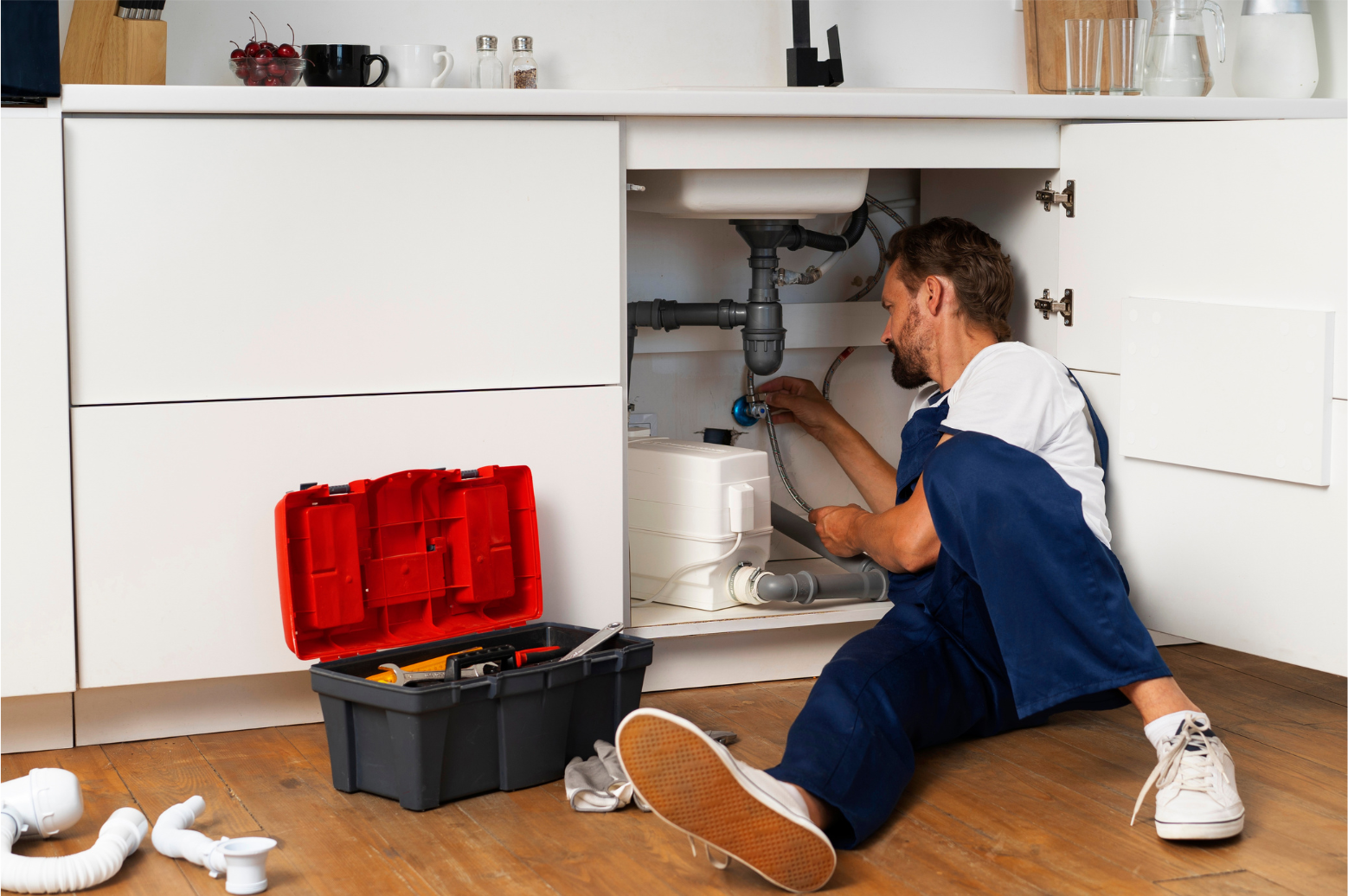 Plumber inspecting under a kitchen sink with tools open on the floor