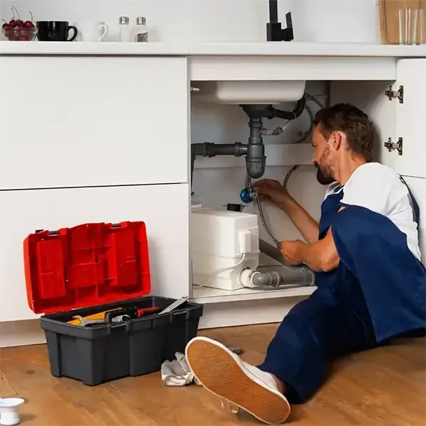 Plumber inspecting under a kitchen sink with tools open on the floor