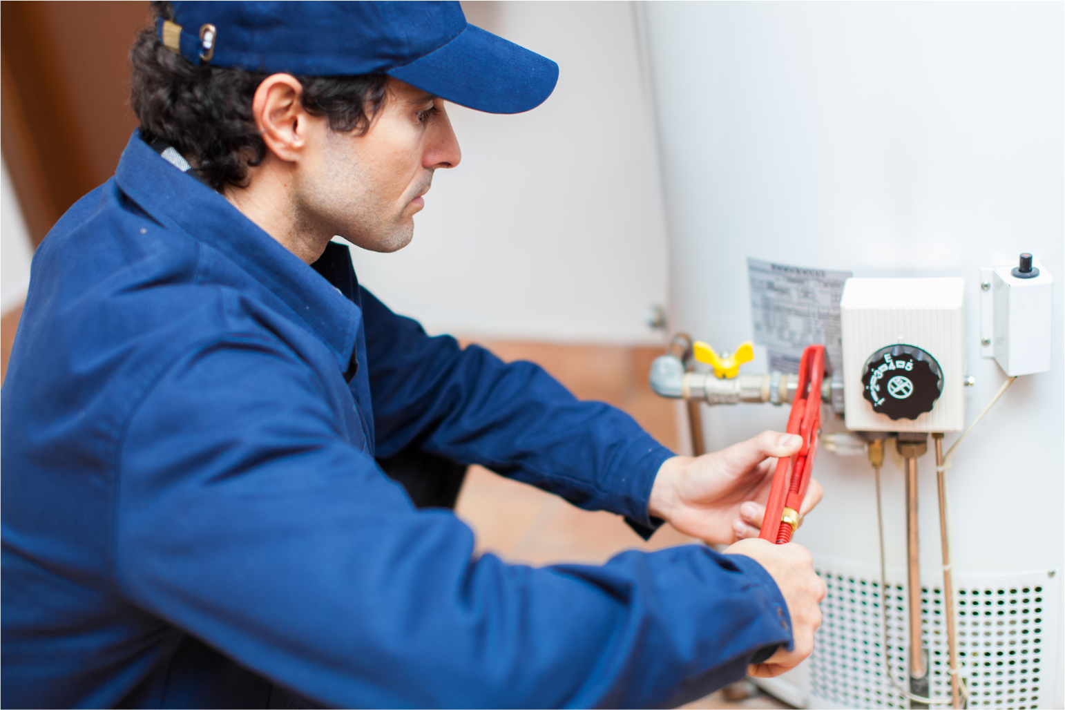 Technician in blue uniform using pliers to work on a wall-mounted electrical panel