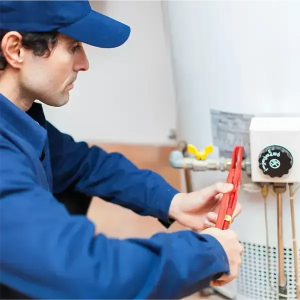 Technician in blue uniform using pliers to work on a wall-mounted electrical panel