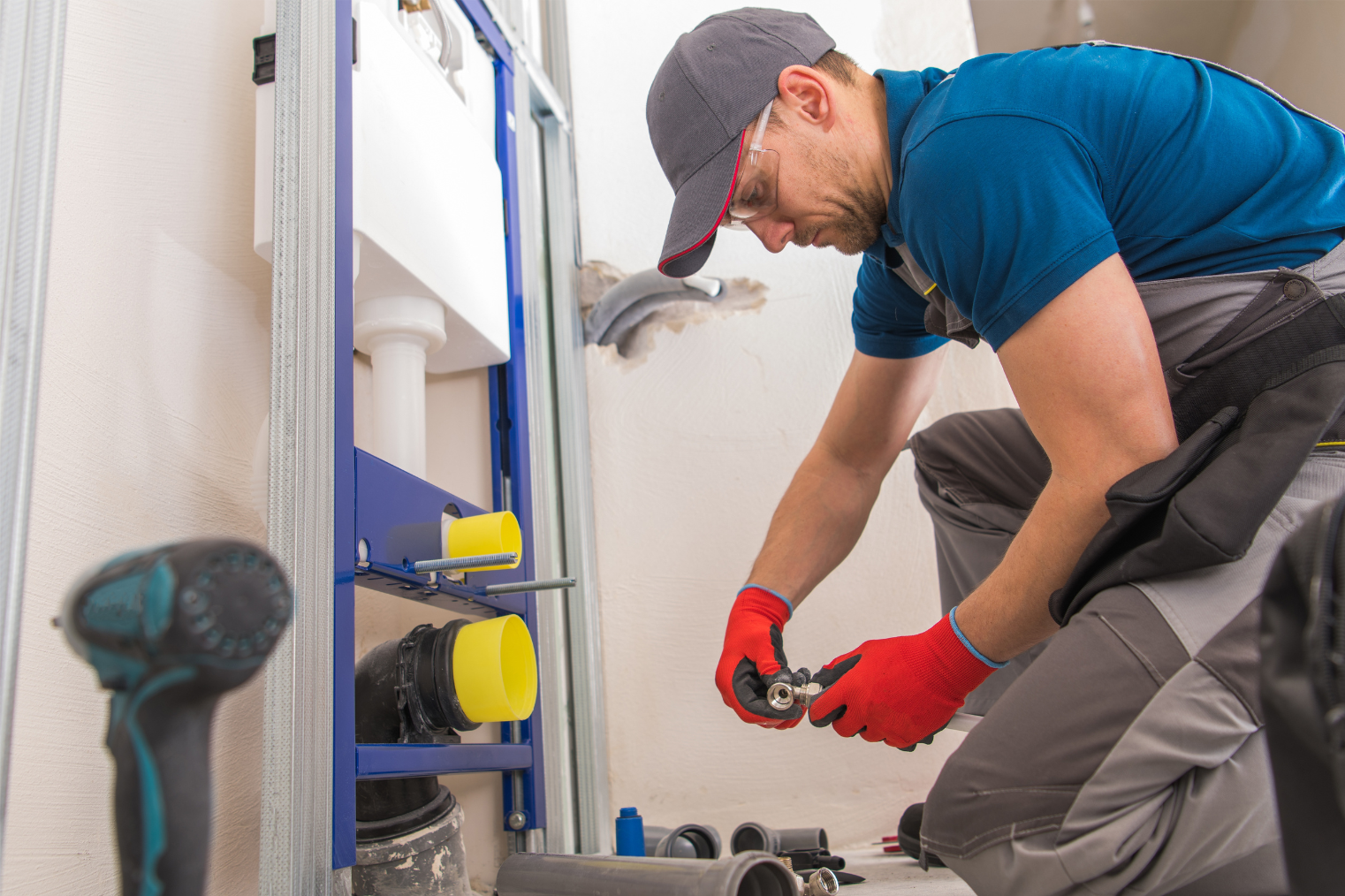 Plumber in red gloves repairing a pipe under a sink in a bathroom or utility room