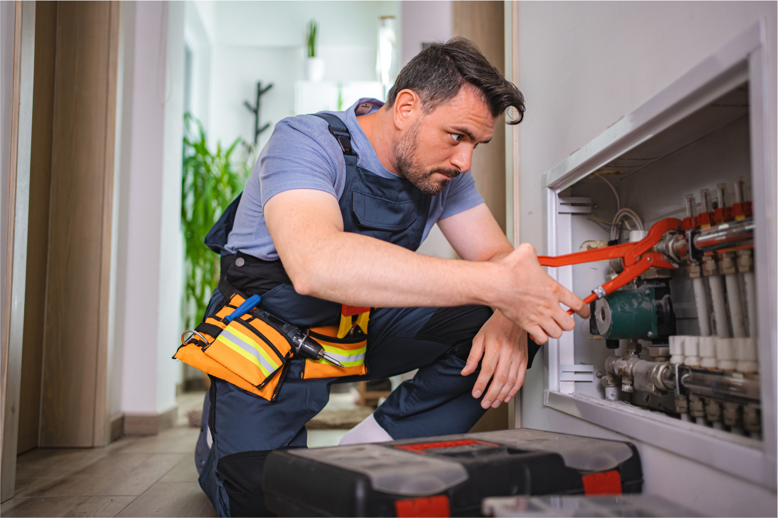 Electrician kneeling by an open breaker panel, tightening wiring in a hallway