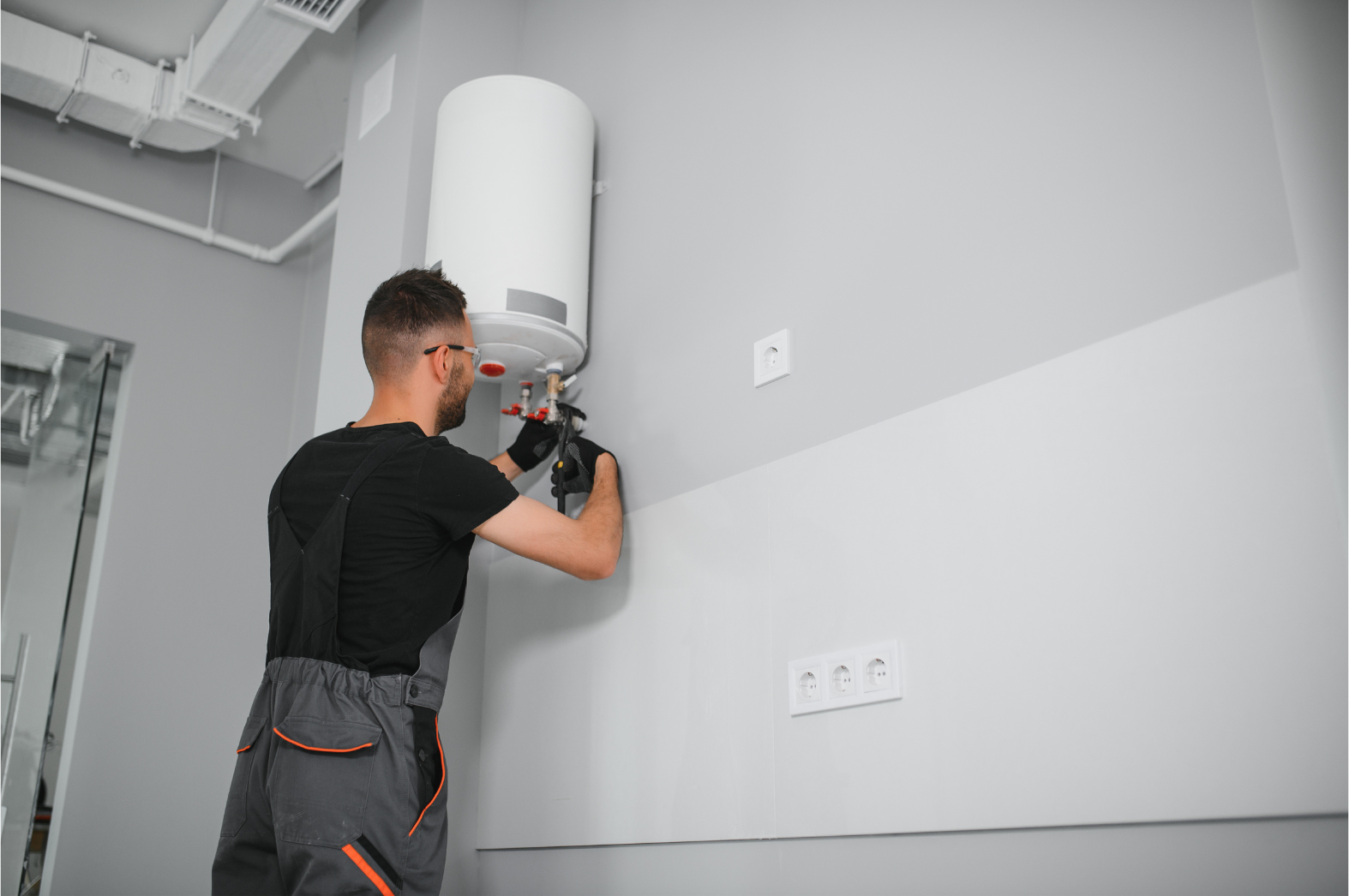 Technician installing a white wall-mounted water heater in a gray utility room