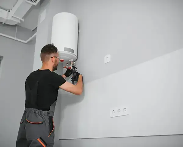 Technician installing a white wall-mounted water heater in a gray utility room