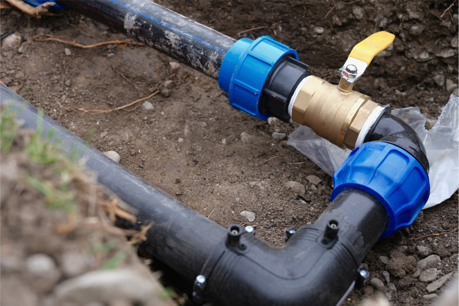 Black and blue PVC pipes joined by brass fittings in a dirt trench