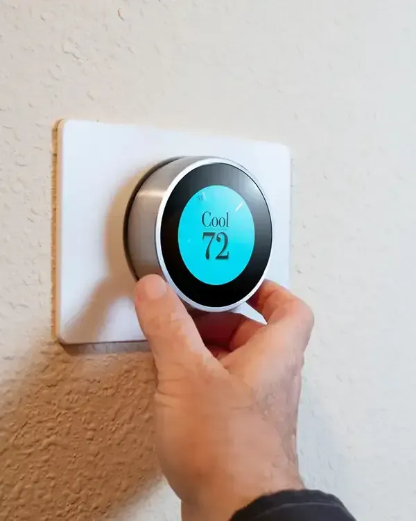 Hand adjusting a round smart thermostat on a wall, display reading 72° and “Cool”
