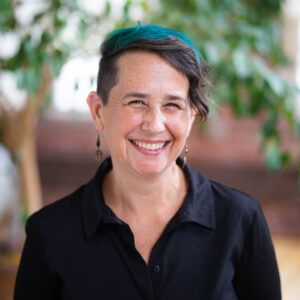 A woman wearing a black shirt and earrings is smiling for the camera.