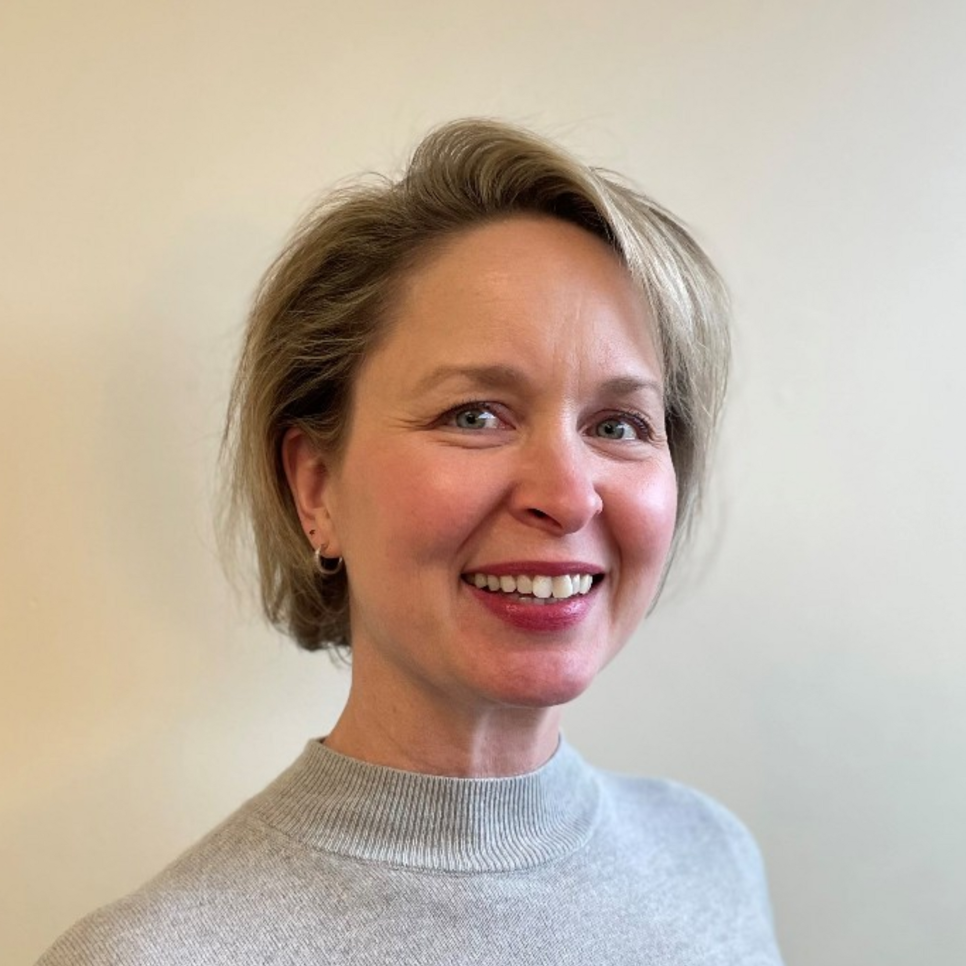A woman in a grey sweater is smiling for the camera.