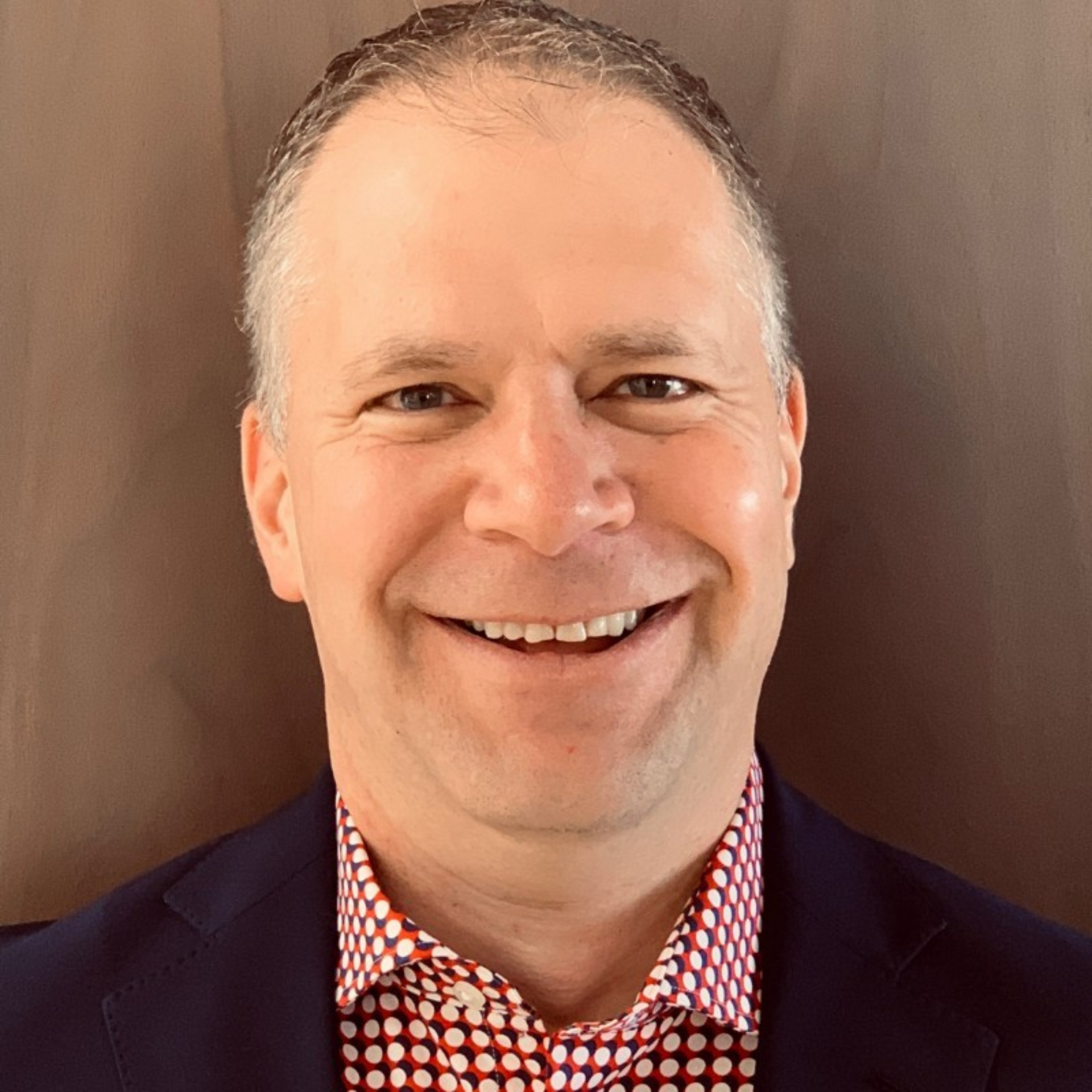 A man in a suit and polka dot shirt is smiling for the camera.