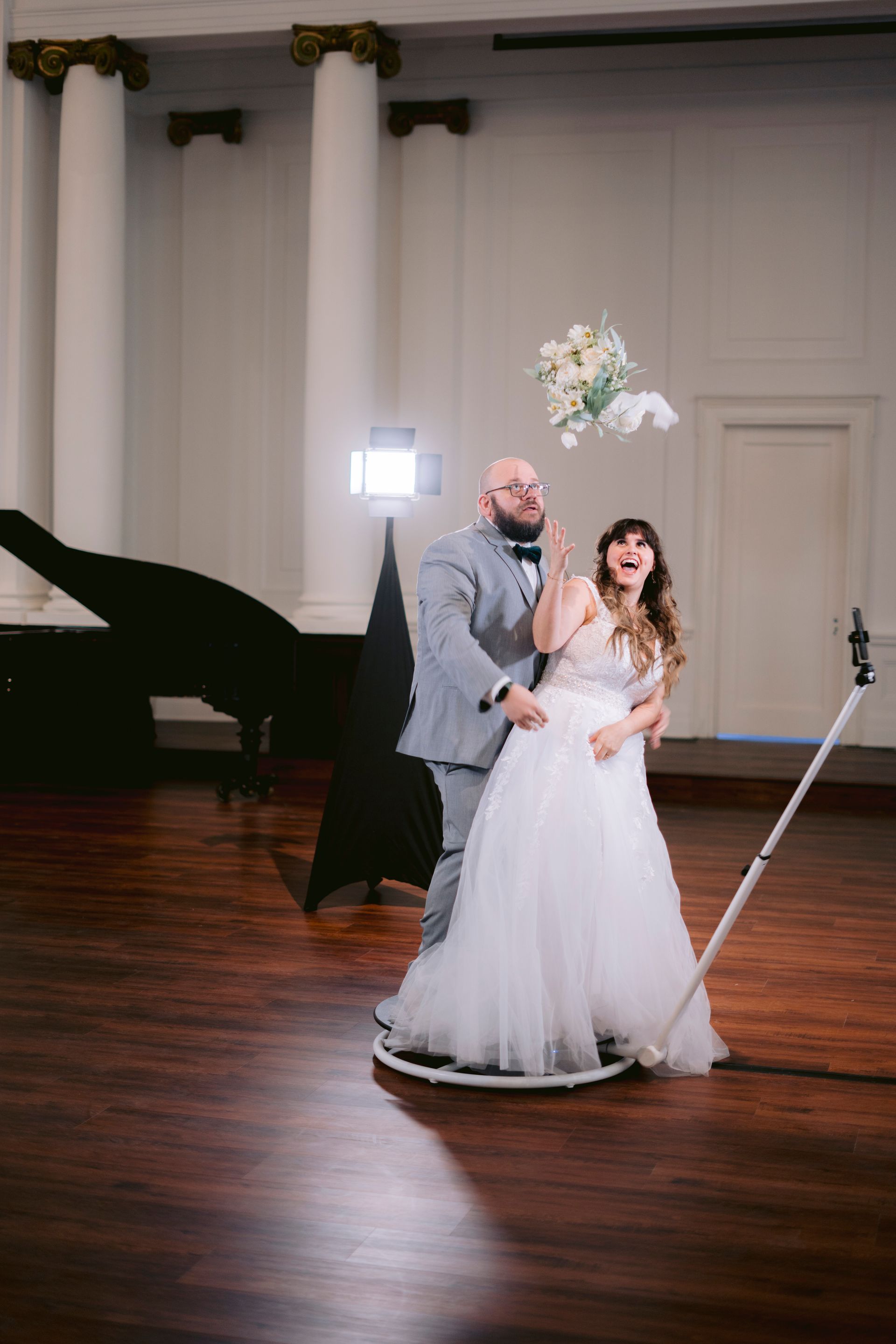 A couple stands on a 360-degree video platform while the bouquet tosses into the air in a grand ballroom.