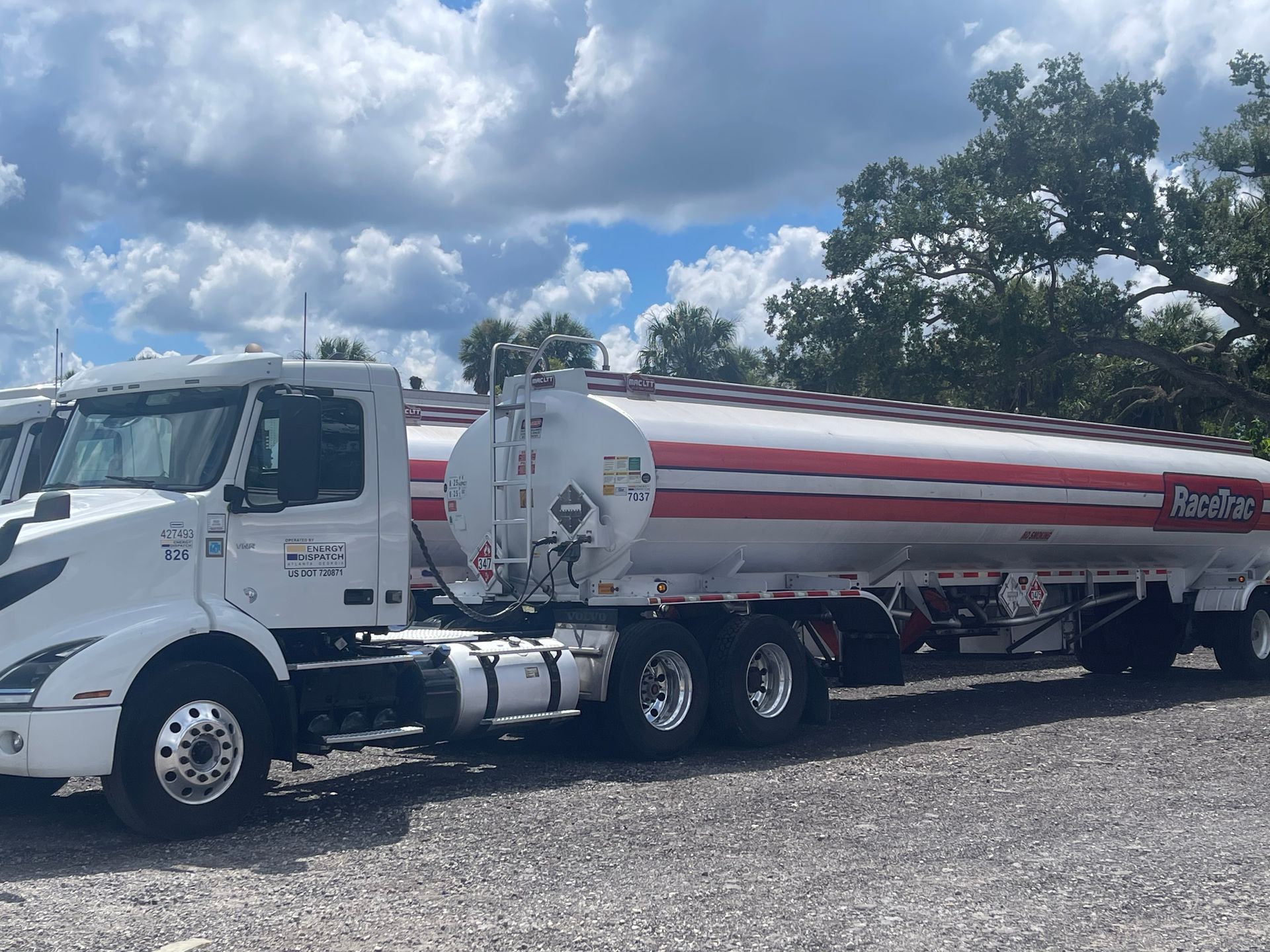 White fuel tanker truck with red stripes parked outdoors under a cloudy sky
