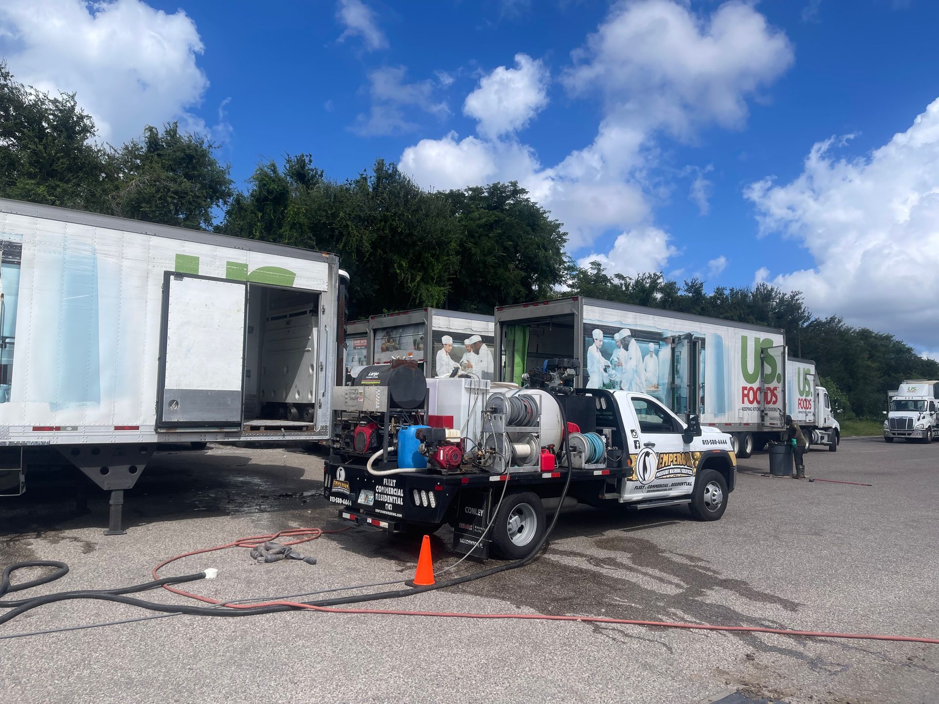 Parking lot with a truck-mounted pressure washer beside box trucks under a partly cloudy sky