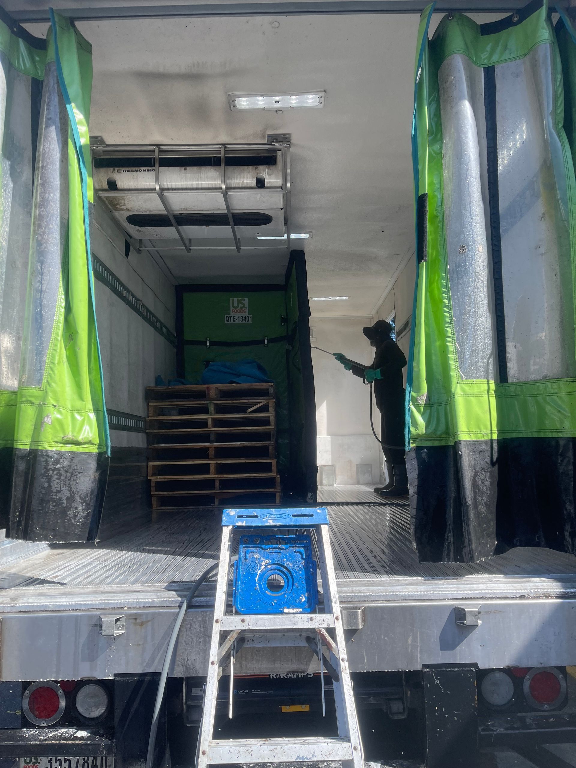 Workers loading cargo into a truck with open rear doors and a blue step stool in the foreground