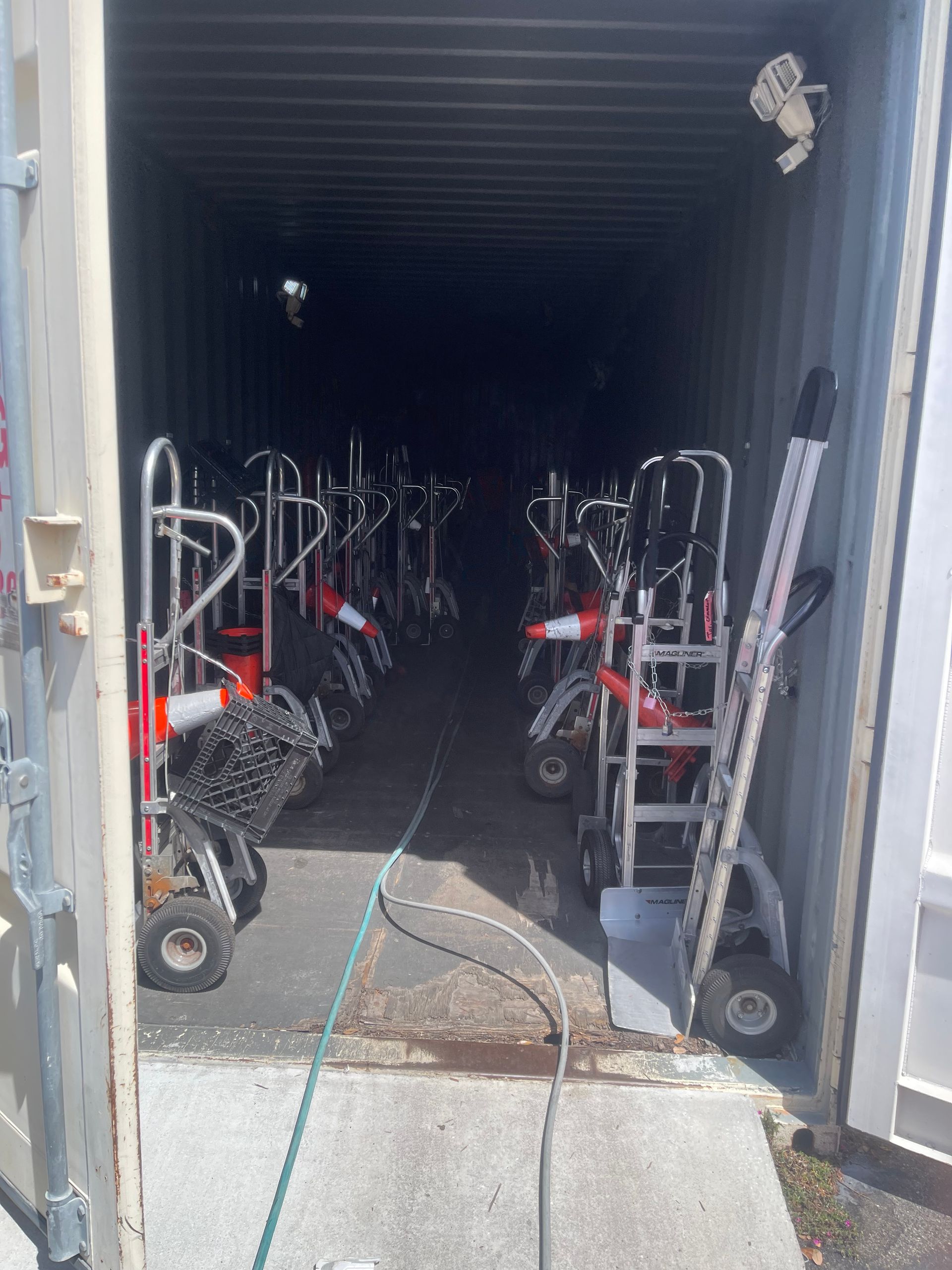 Storage container filled with rows of mobility scooters, viewed through open doors from a concrete ramp