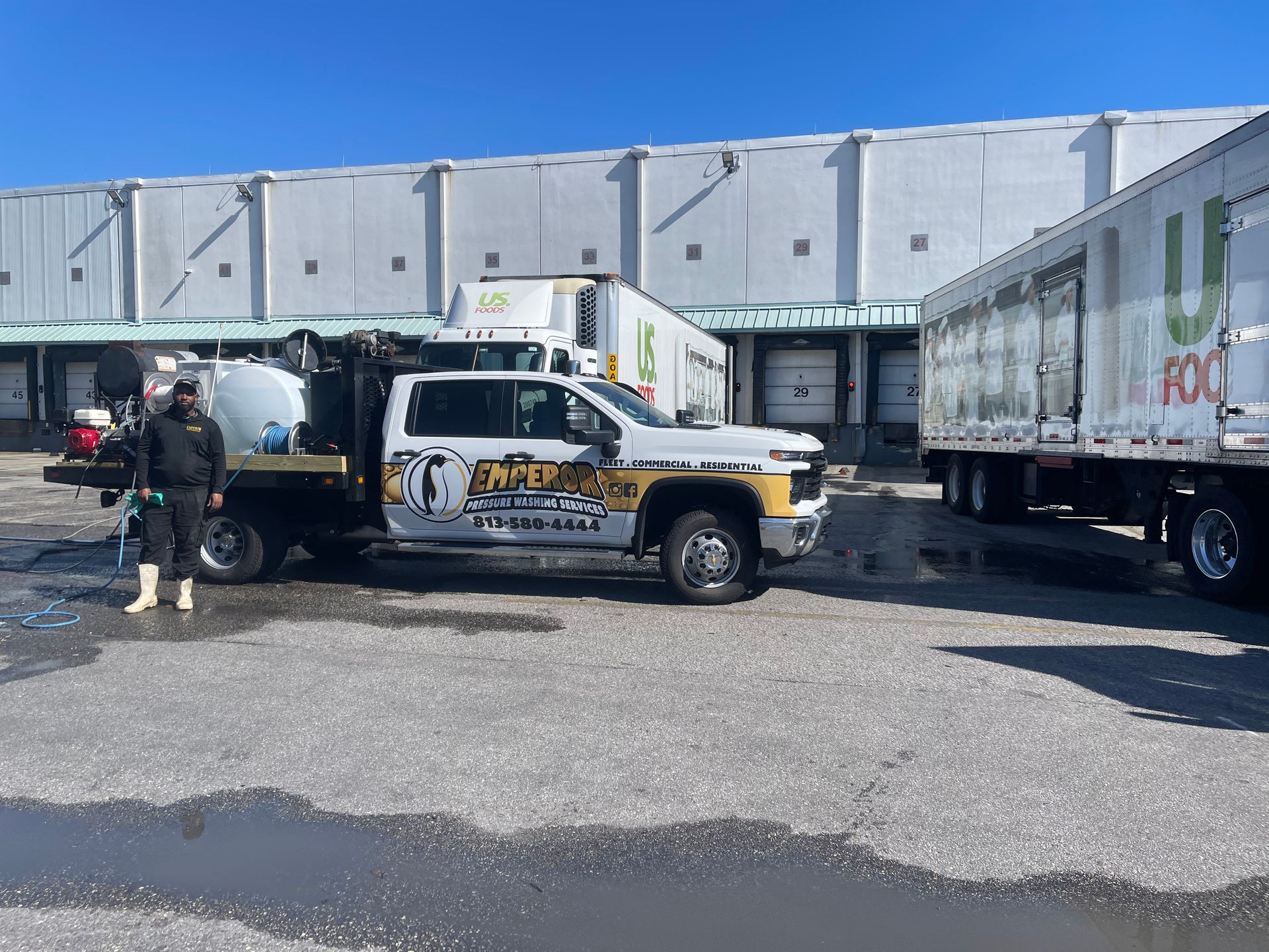 Tow truck and box trucks parked in an industrial lot under a loading dock.