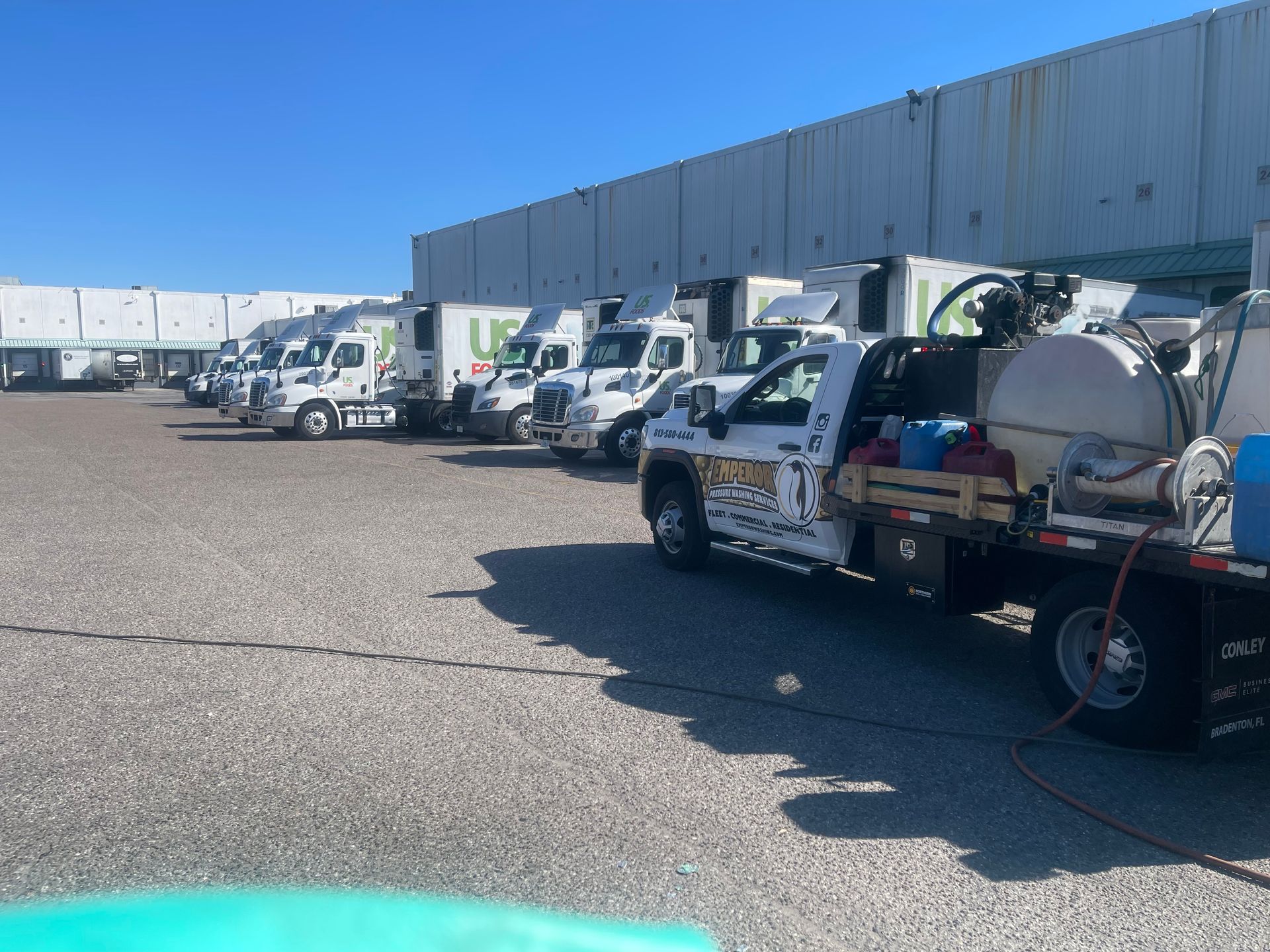 Line of white utility trucks parked beside a long warehouse under a clear blue sky.