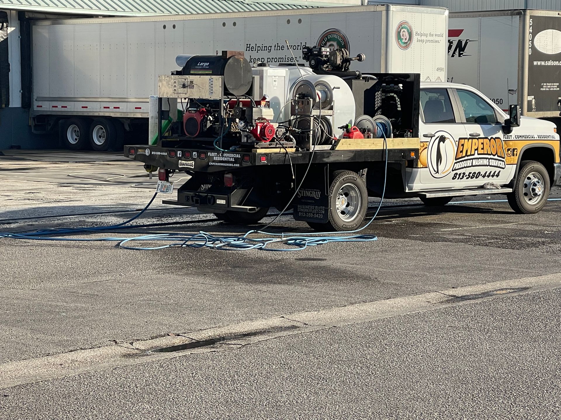 White pickup truck with mounted machinery parked in a lot beside a semi-trailer