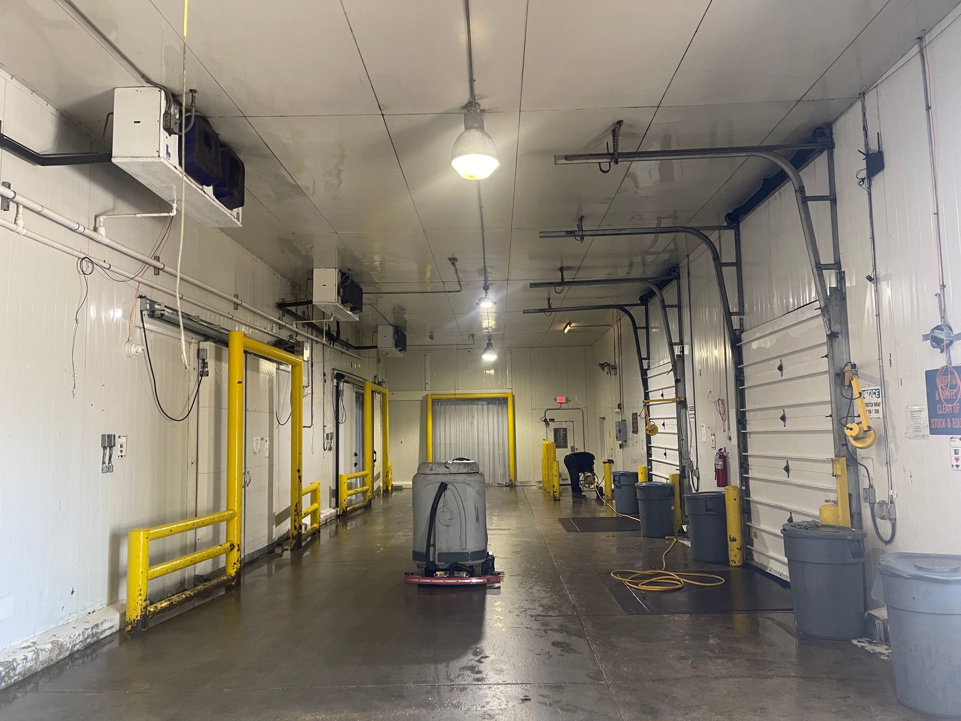 Interior of a car wash bay with a cart on the wet floor and yellow safety rails along the wall.