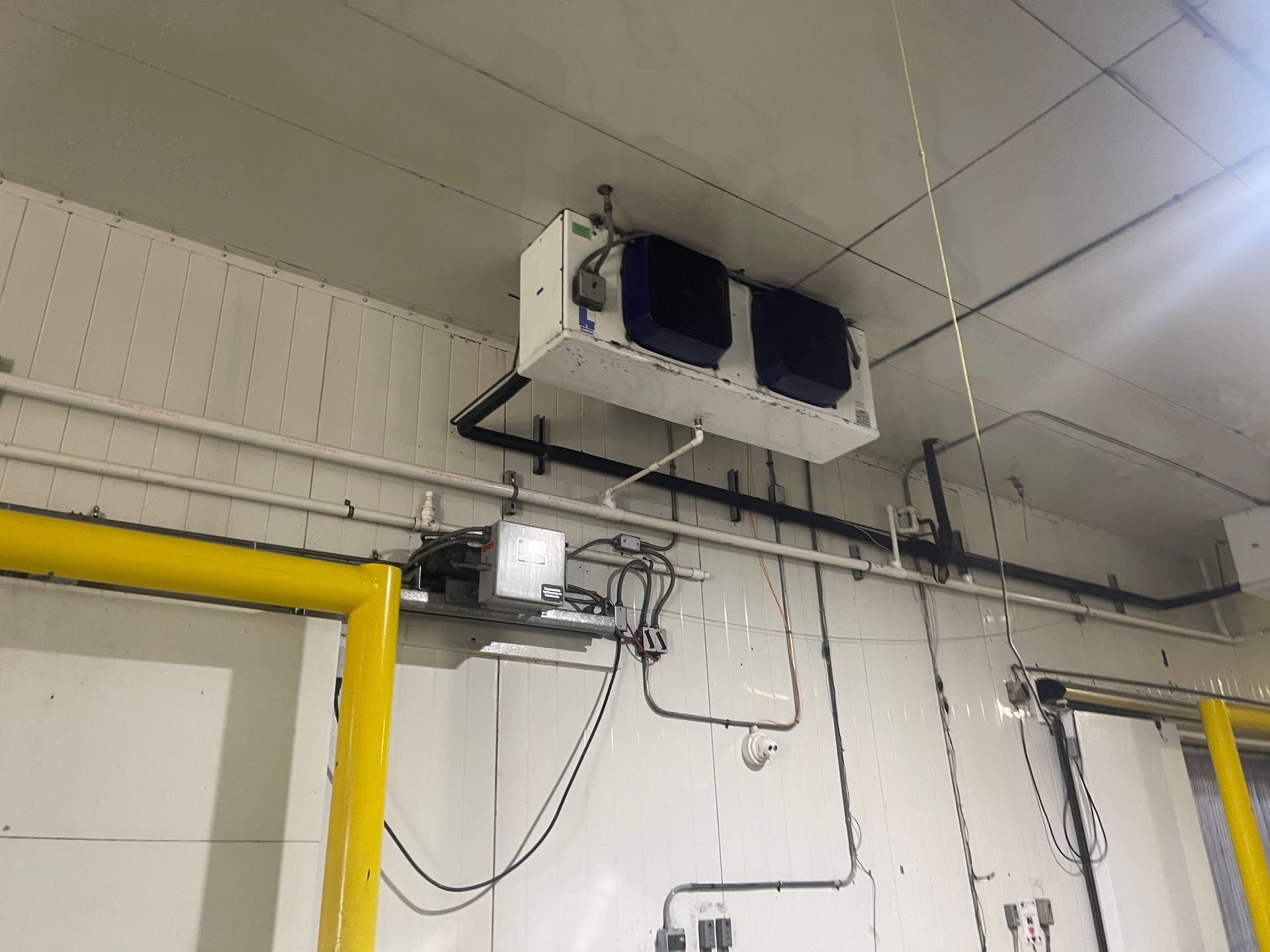 Industrial ceiling-mounted HVAC unit and wiring in a utility room with yellow trim and white walls