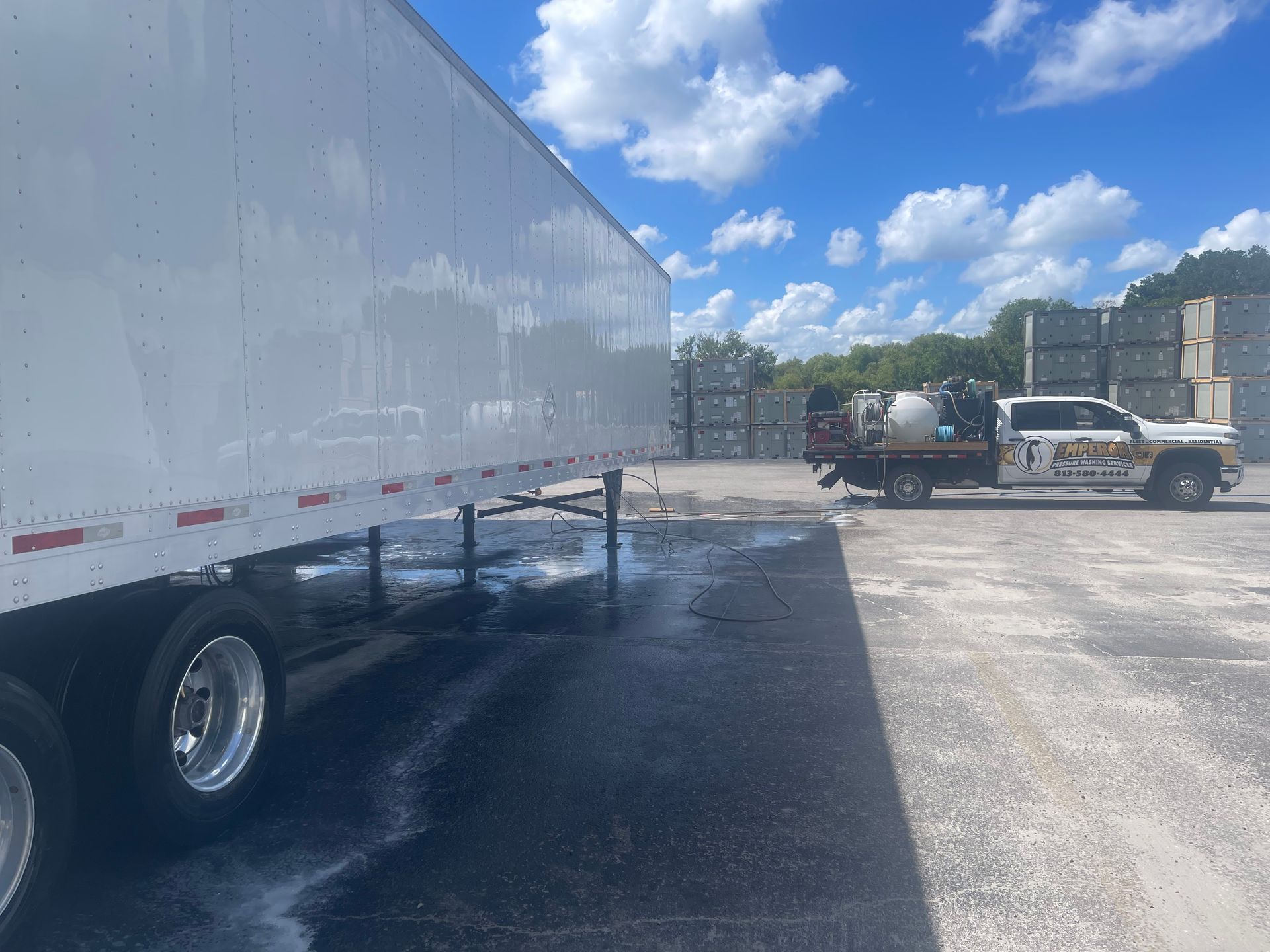 White semi-truck trailer parked on a gravel lot under a blue, partly cloudy sky