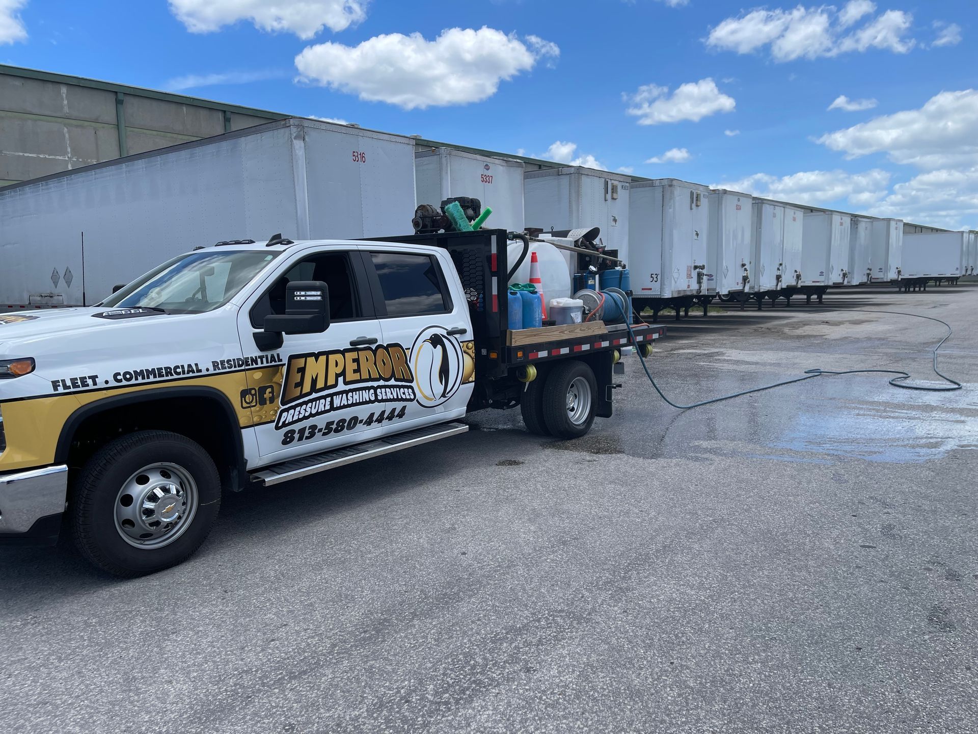 White work truck with equipment parked beside warehouse trailers under a blue sky