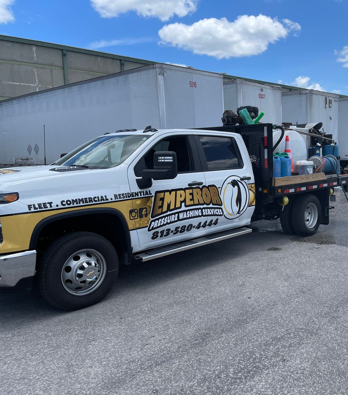 White and gold service truck with tools parked beside a warehouse on a sunny day