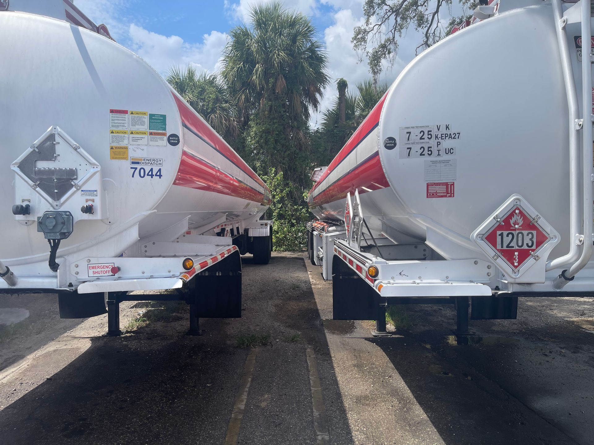 Two white fuel tanker trailers parked side by side on a gravel lot under a cloudy sky