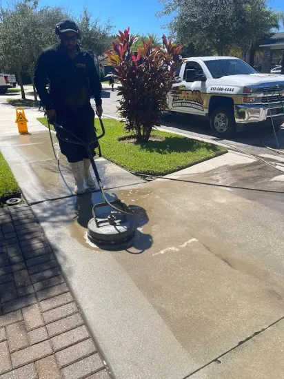 Person using a sidewalk cleaner on a sunny residential sidewalk, with a truck parked nearby.