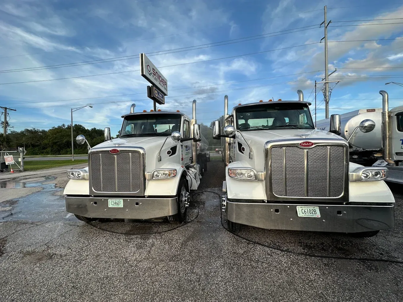 Two white semi trucks parked side by side on a wet lot under a cloudy sky