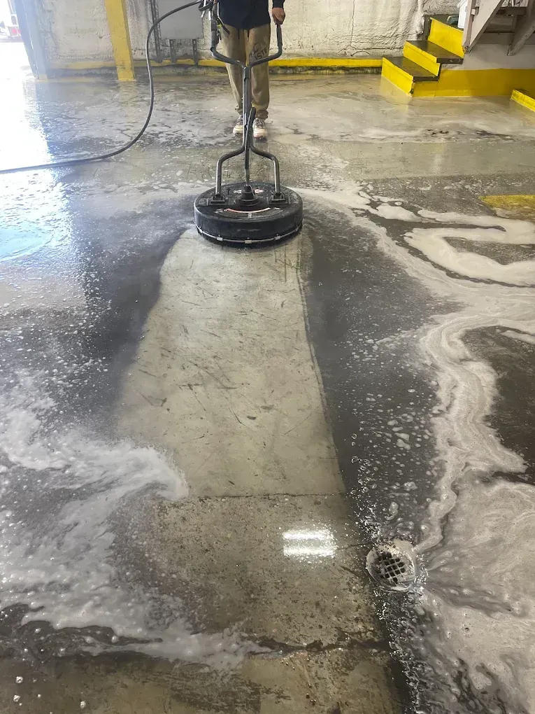 Worker cleaning a wet concrete floor with a rotary scrubber in an industrial space