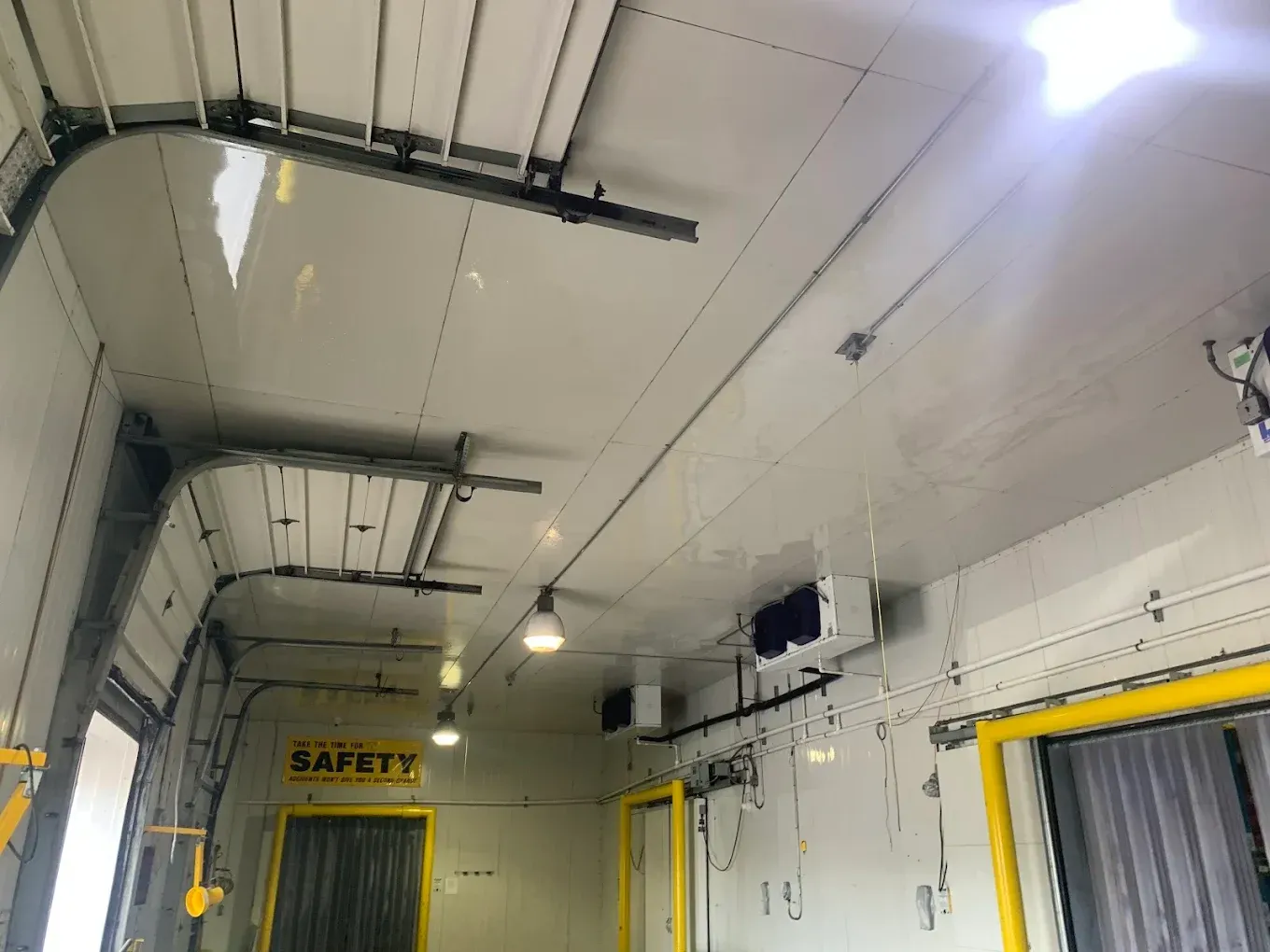Industrial loading bay with white ceiling, yellow door frames, and a safety sign above the doorway