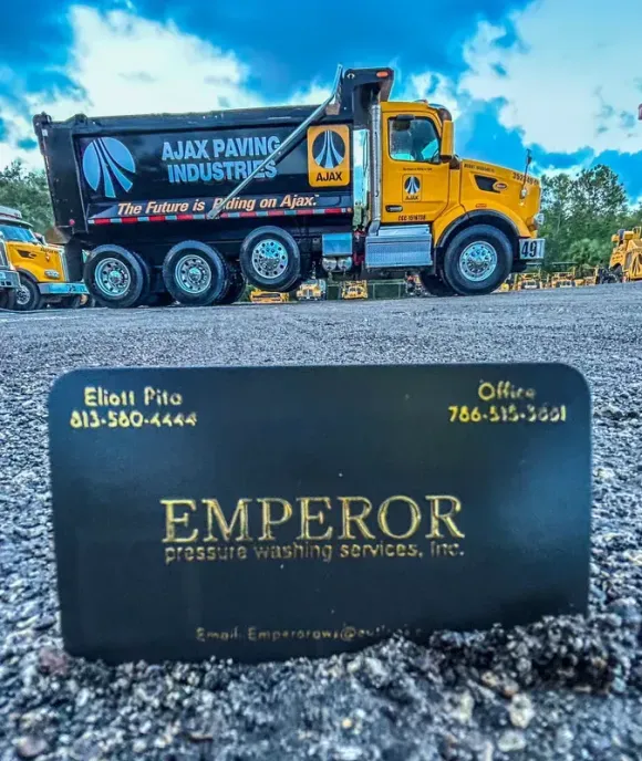 Yellow-and-black paving truck behind an Emperor business card on gravel