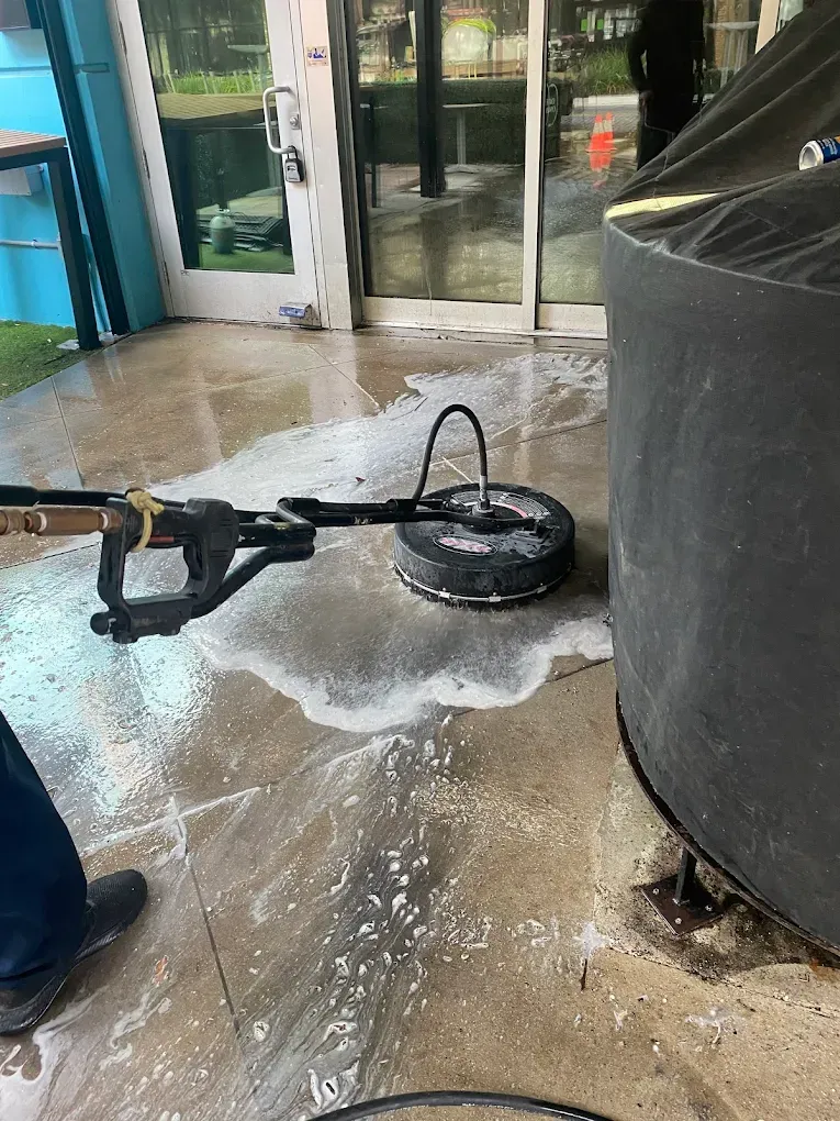 A robot vacuum lies on a wet floor beside a large gray cylinder near glass doors.